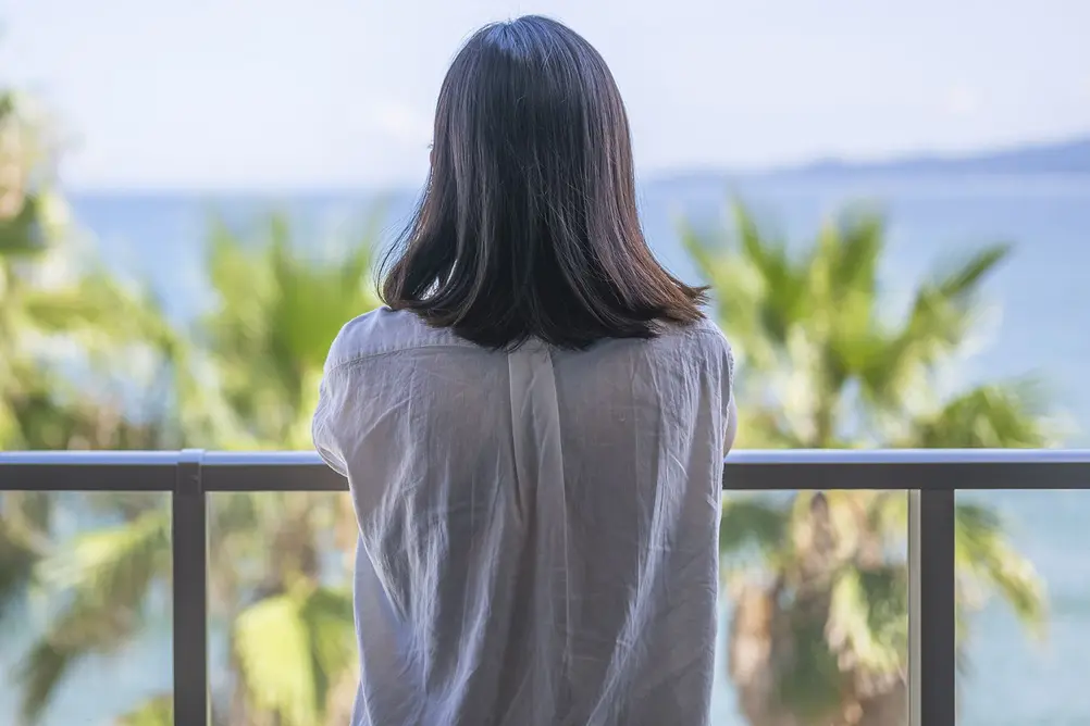 زن در تعطیلات کنار دریا، در حال آرامش و نگاه به دریا از بالکن، در فوکوئوکا، ژاپن - تصویر استوک