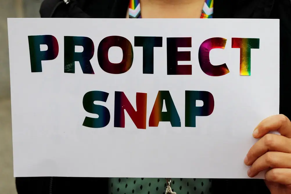 زنی که تابلویی با نوشته «از برنامه SNAP محافظت کنید» در دست دارد.